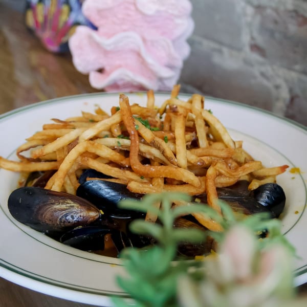 Lighthouse Coastal Brasserie's mussels and fries, with a decorative pink shell in the background.