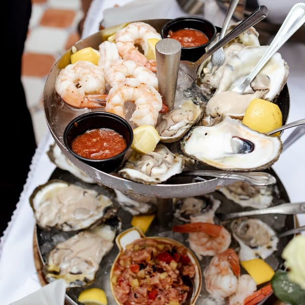 A two-tiered seafood tower with oysters, shrimp, cocktail sauce, and lemon wedges on ice.
