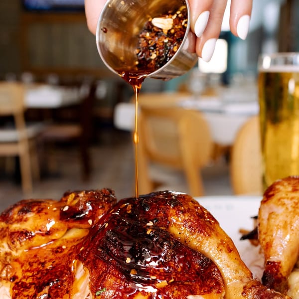 A hand pours chili oil from a metal cup onto a roasted chicken dish at Lighthouse Coastal Brasserie.