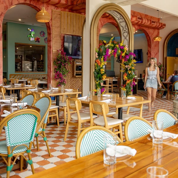 Lighthouse Coastal Brasserie's vibrant dining room with patterned chairs, wooden tables, and a woman walking through.