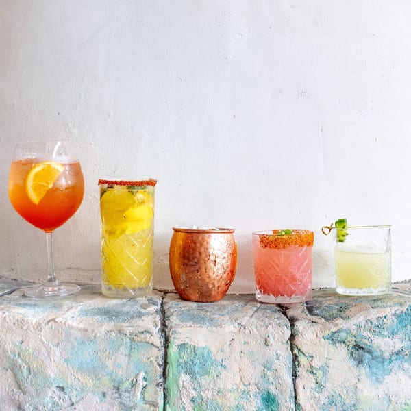 Five colorful cocktails, including an Aperol Spritz, on a textured blue and white surface.