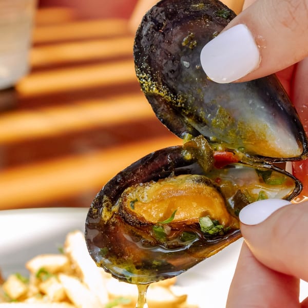 A hand with white fingernails holds open a mussel, revealing the succulent seafood inside.